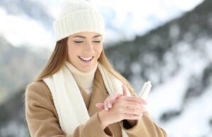 Trockene Haut im Winter: junge Frau vor winterlicher Kulisse cremt sich die Hände ein